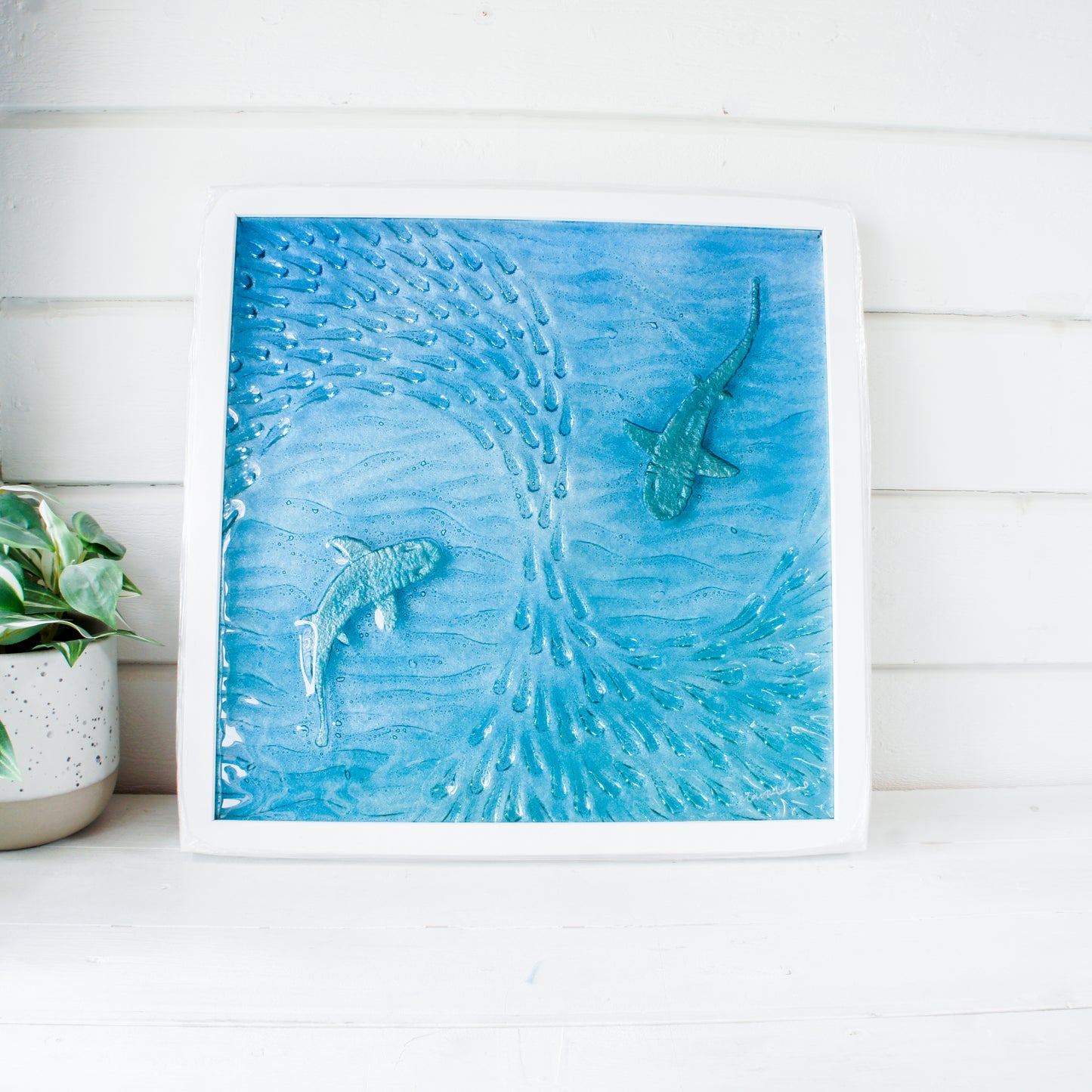 Framed artwork of dolphins swimming in water on a white wall.