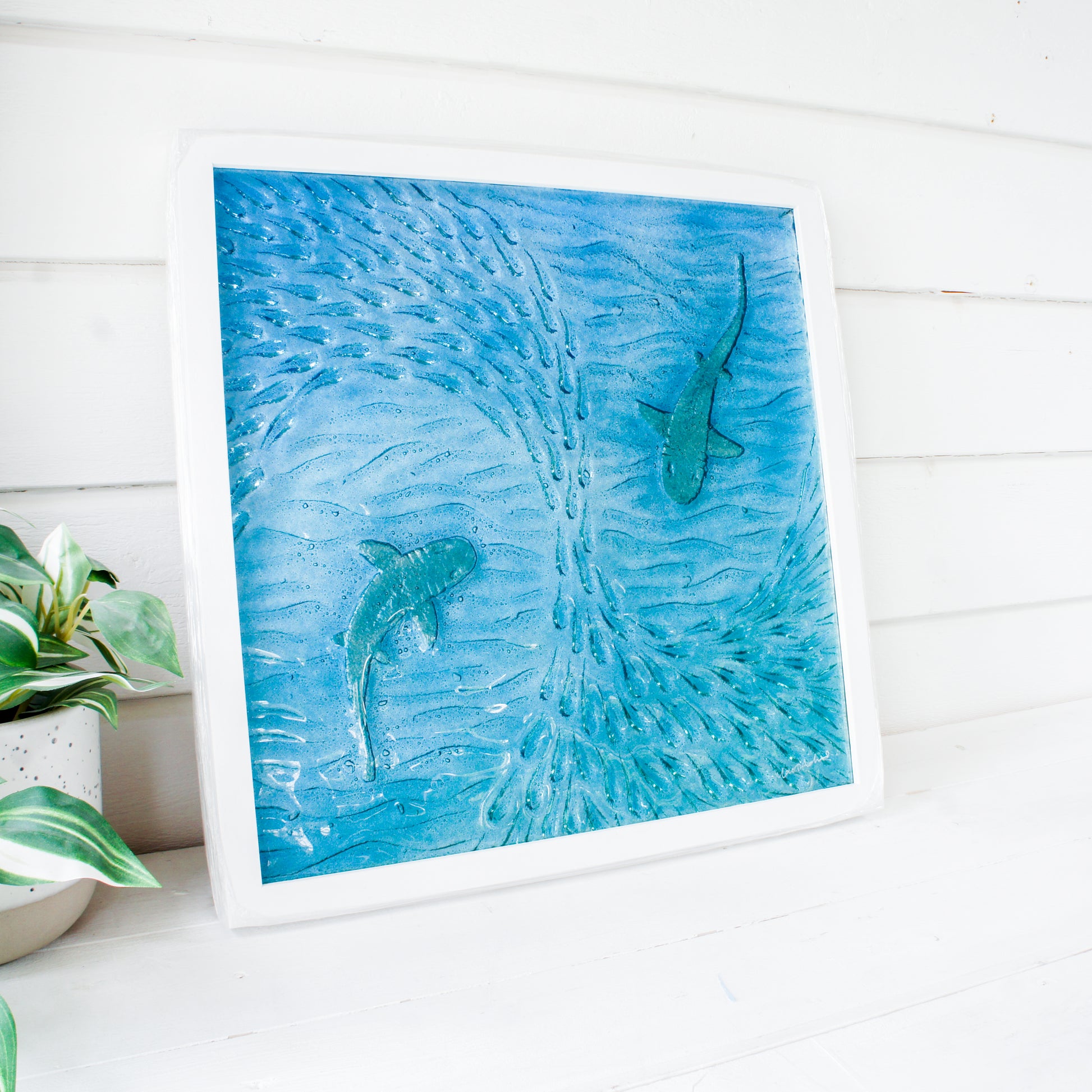2 silver sharks swimming in blue teal turquoise sea with shoal of fish textured fused glass in square white wooden frame 45cm, ready to hang