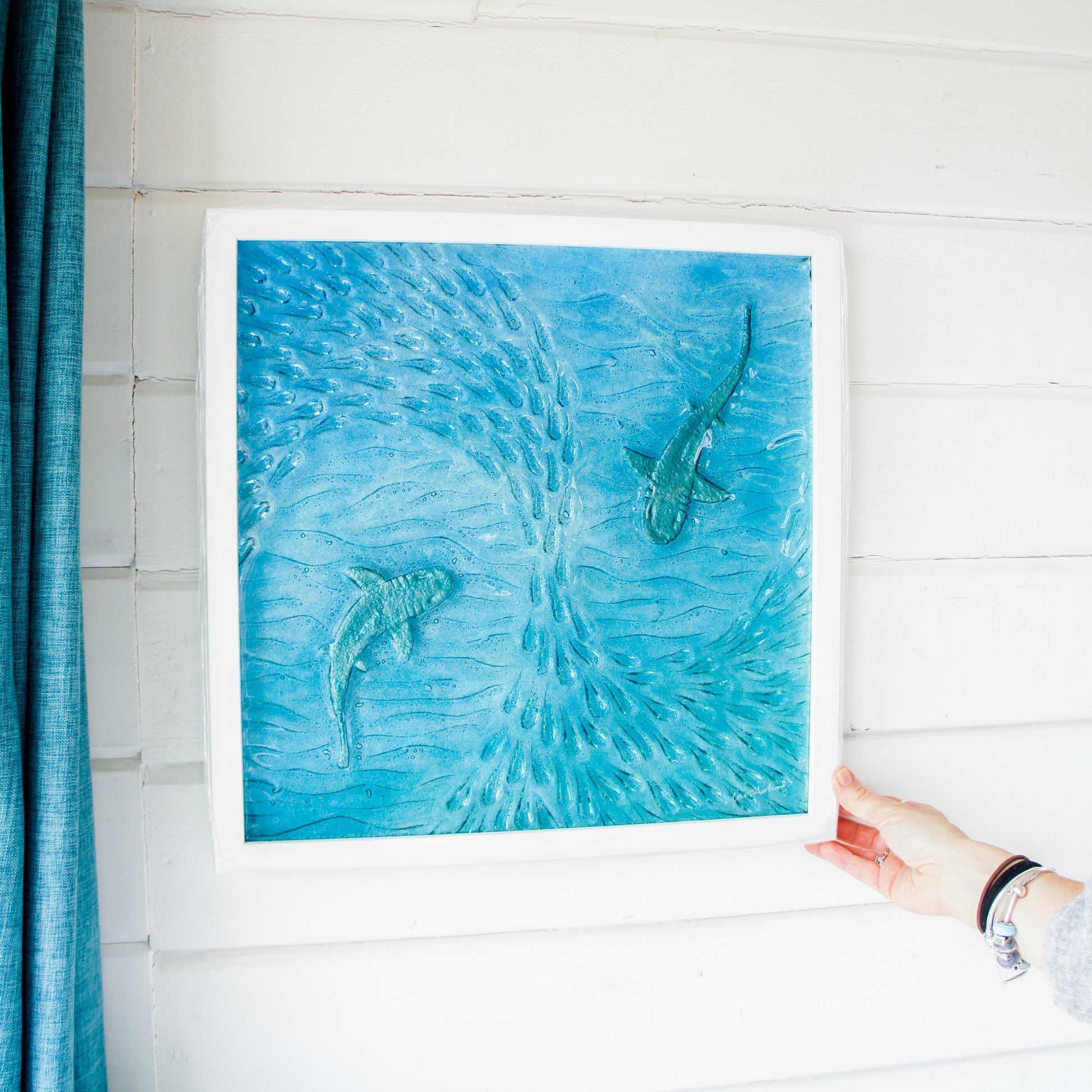 2 silver sharks swimming in blue teal turquoise sea with shoal of fish textured fused glass in square white wooden frame 45cm, ready to hang