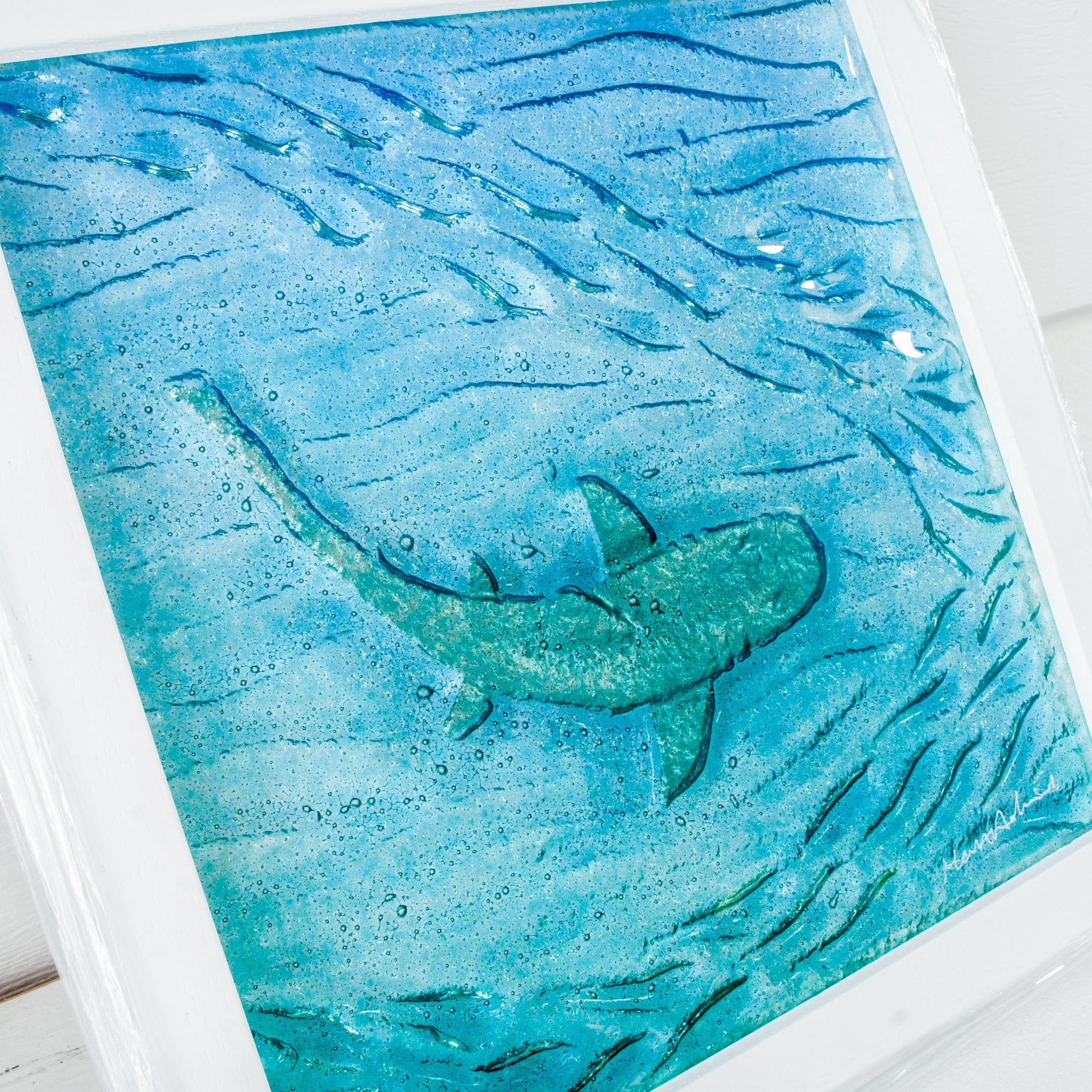 silver shimmering shark swimming in turquoise blue water with shoal of fish in textured fused glass in a white wooden frame 25x25cm (10")