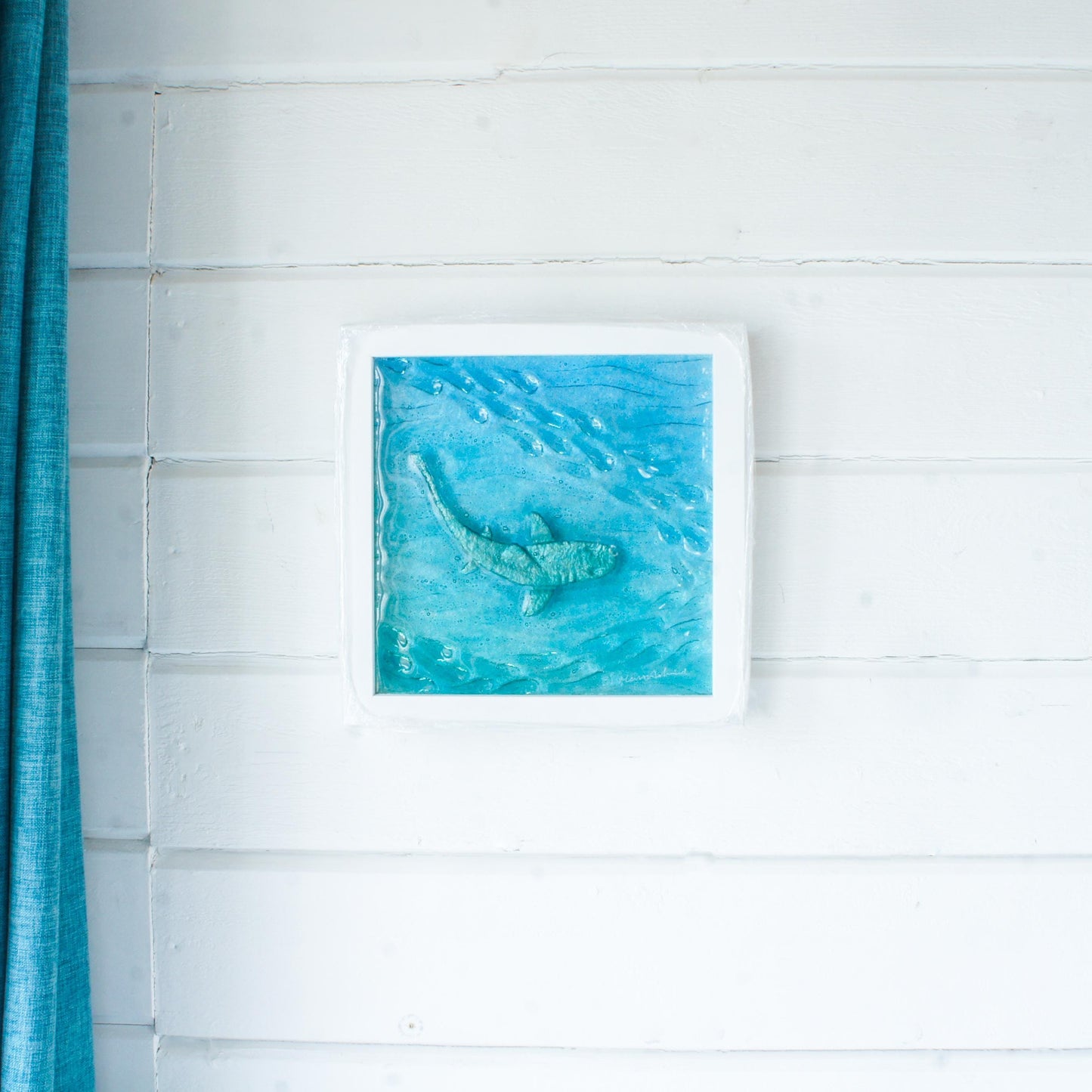 silver shimmering shark swimming in turquoise blue water with shoal of fish in textured fused glass in a white wooden frame 25x25cm (10")