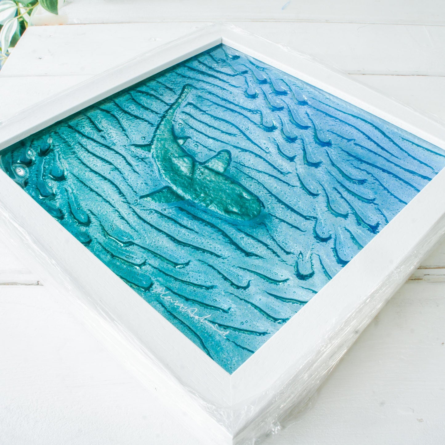 silver shimmering shark swimming in turquoise blue water with shoal of fish in textured fused glass in a white wooden frame 25x25cm (10")