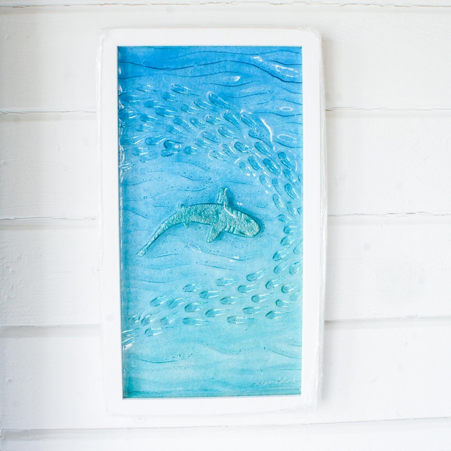 shark painted in silver swimming wideway with fish in blue sea fused glass wall art in a white wooden frame 25x45cm