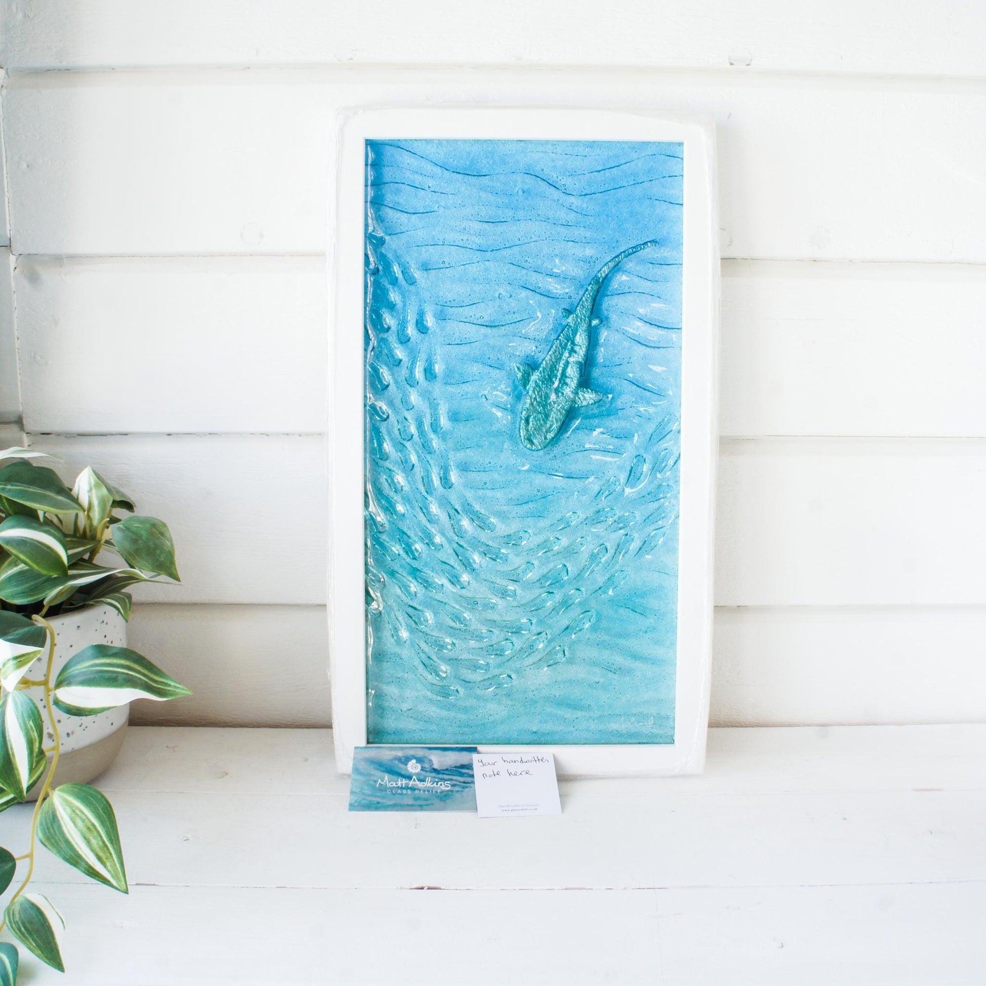 shark painted in silver swimming down with fish in blue sea fused glass wall art in a white wooden frame 25x45cm with gift note and business card