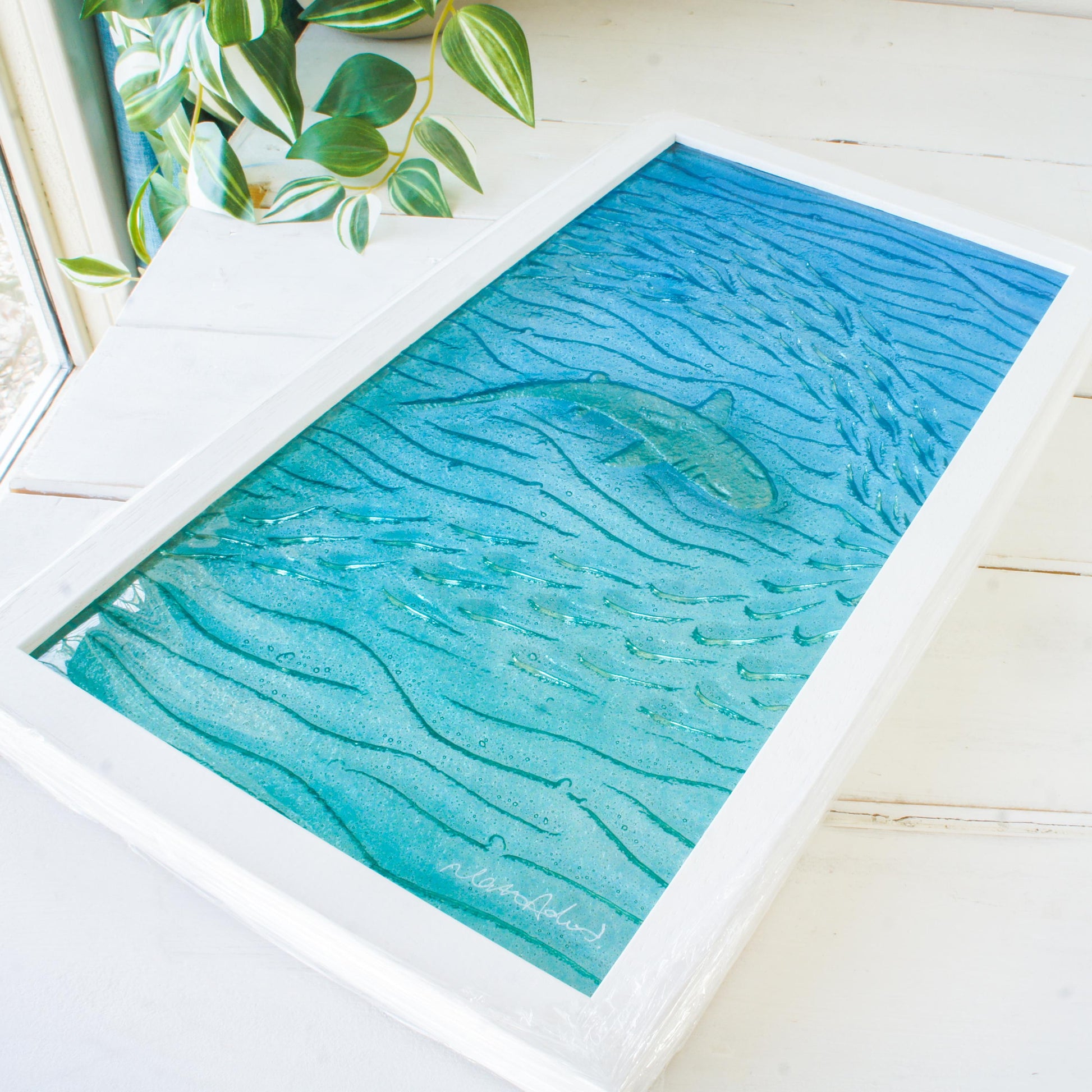 shark painted in silver swimming wideway with fish in blue sea fused glass wall art in a white wooden frame 25x45cm, view from bottom