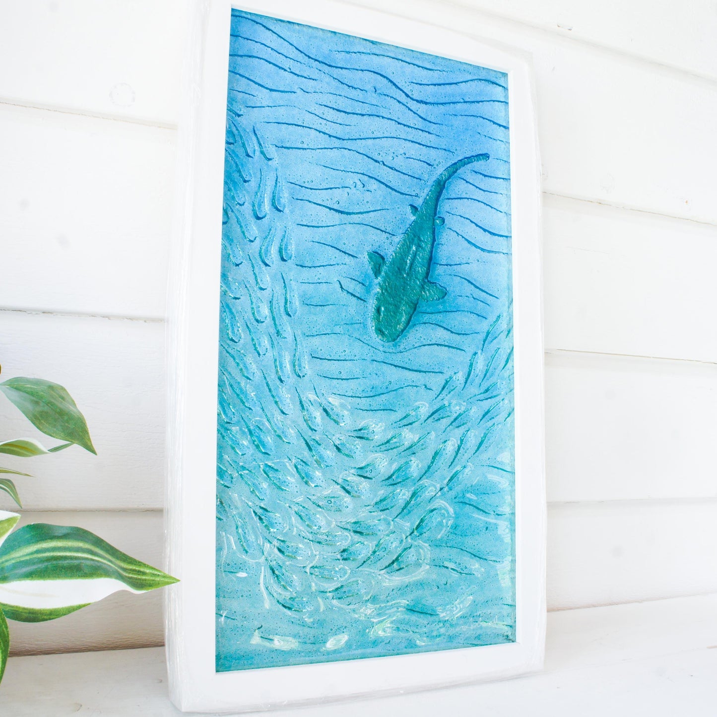 shark backpainted in silver swimming down with fish in blue sea fused glass wall art in a white wooden frame 25x45cm view from side