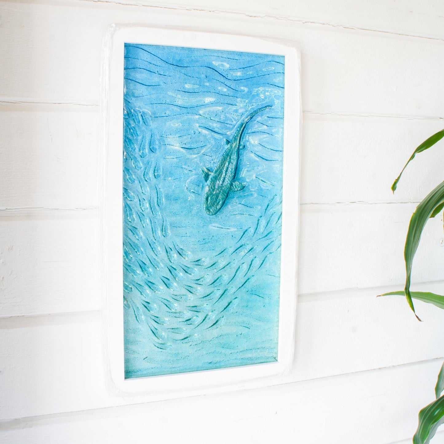 view from side of shark in silver swimming around fish in blue and turquoise ocean with textured fused glass, portrait shape framed in and ready to hang 25x45cm