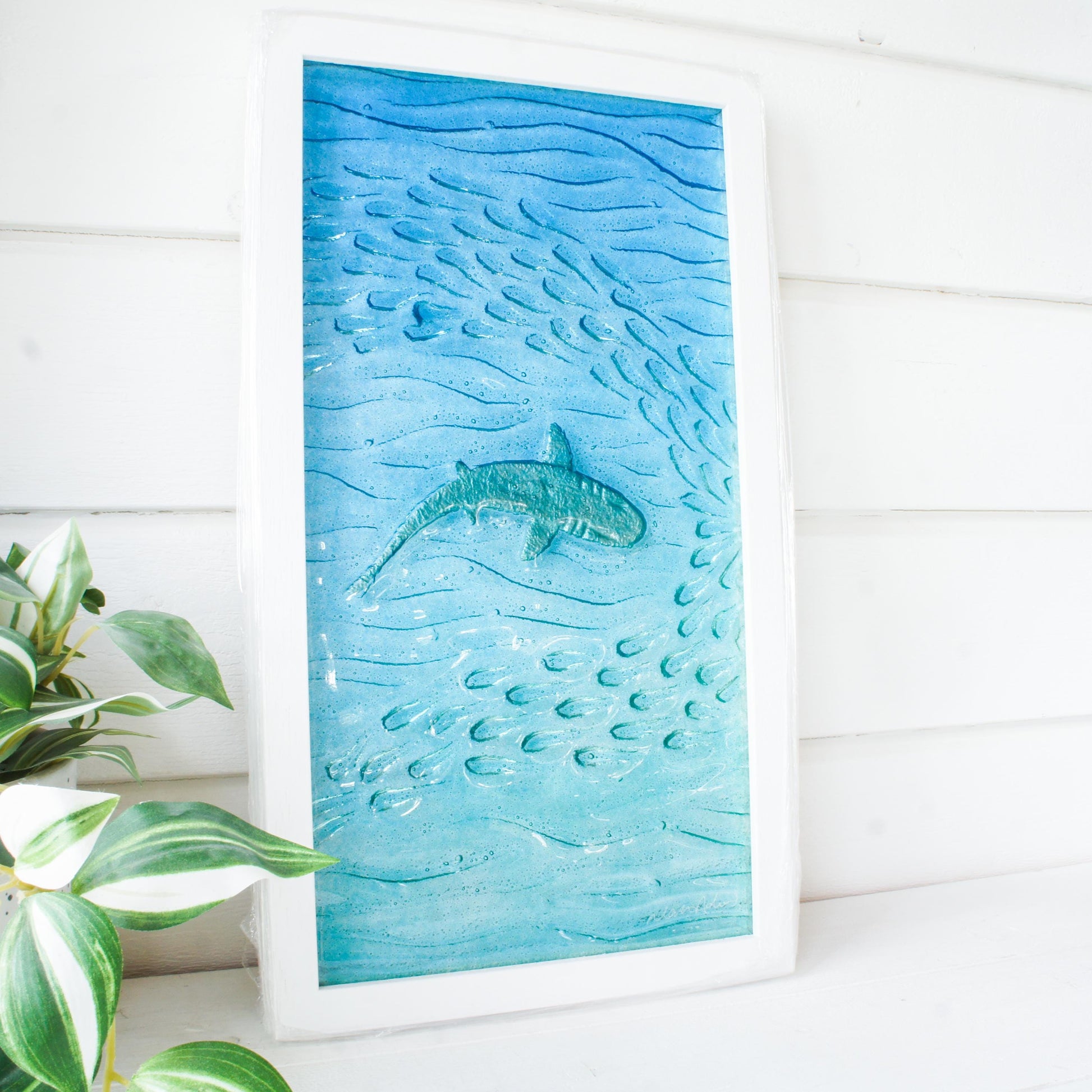 shark painted in silver swimming wideway with fish in blue sea fused glass wall art in a white wooden frame 25x45cm